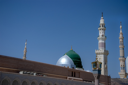 View of Al Masjid e Nabawi with its iconic green dome and tall minarets against a clear blue sky in Madinah Al Madinah Province Saudi Arabia.