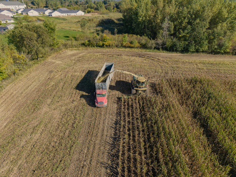 Green Bay Wisconsin United States 25 September 2026 Aerial view of a combine harvester chopping corn for silage and loading it into a trailer in a rural field.