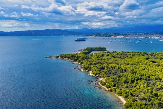 Aerial view of Ile Sainte Marguerite featuring dense pine forests rocky shores and turquoise waters with a cruise ship and boats in the bay of Cannes Provence Alpes Cote d Azur France. Aerial view of Ile Sainte Marguerite featuring dense pine forests rocky shores and turquoise waters with a cruise ship and boats in the bay of Cannes Provence Alpes Cote d Azur France.