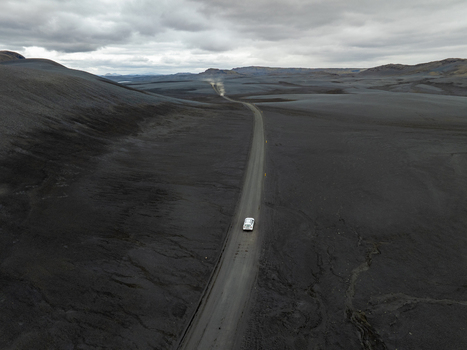 Aerial view of a car driving along a winding road through a vast dark volcanic landscape under an overcast sky in Iceland. Aerial view of a car driving along a winding road through a vast dark volcanic landscape under an overcast sky in Iceland.