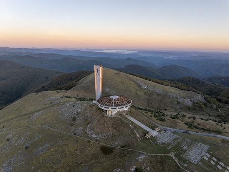 Aerial view of the Buzludzha Monument a brutalist structure on a mountain peak surrounded by rolling hills under a soft sunset sky in Stara Zagora Bulgaria. Aerial view of the Buzludzha Monument a brutalist structure on a mountain peak surrounded by rolling hills under a soft sunset sky in Stara Zagora Bulgaria.