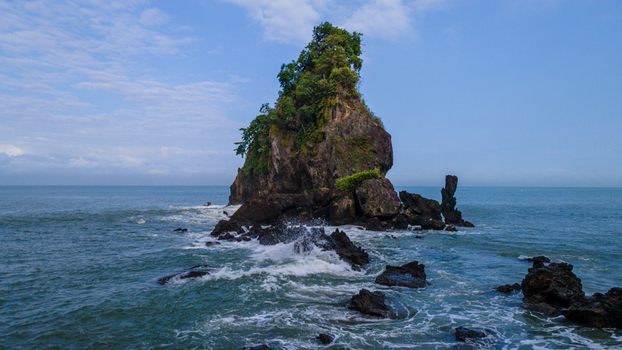 Aerial view of the Karang Agung Beach rock formation covered in greenery with waves crashing against the rugged coast Ayah Central Java Indonesia. Aerial view of the Karang Agung Beach rock formation covered in greenery with waves crashing against the rugged coast Ayah Central Java Indonesia.