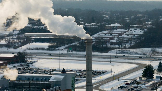 Aerial view of an industrial smokestack emitting white steam over a snow covered landscape with a highway and residential buildings in Reading Ohio United States. Aerial view of an industrial smokestack emitting white steam over a snow covered landscape with a highway and residential buildings in Reading Ohio United States.
