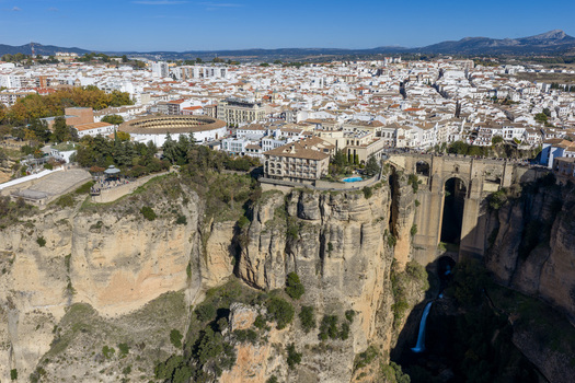 Aerial view of the historic Puente Nuevo bridge spanning the deep El Tajo gorge with the white buildings of Ronda town and the bullring in the background Ronda Andalusia Spain. Aerial view of the historic Puente Nuevo bridge spanning the deep El Tajo gorge with the white buildings of Ronda town and the bullring in the background Ronda Andalusia Spain.