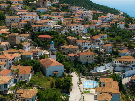 Aerial view of the traditional stone houses and terracotta roofs of a hillside village featuring a white church with a blue dome in Dhermi Vlore County Albania. Aerial view of the traditional stone houses and terracotta roofs of a hillside village featuring a white church with a blue dome in Dhermi Vlore County Albania.