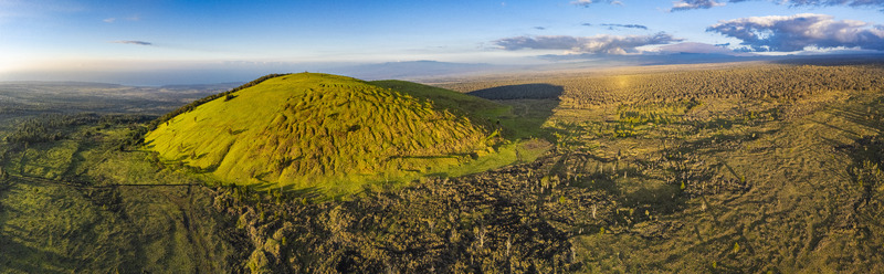Aerial view of Puu Waawaa cinder cone surrounded by dark lava fields and green vegetation under a clear sky Hawaii County Hawaii United States. Aerial view of Puu Waawaa cinder cone surrounded by dark lava fields and green vegetation under a clear sky Hawaii County Hawaii United States.