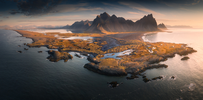 Aerial view of the sharp Vestrahorn mountain peaks and Stokksnes peninsula with black sand beaches and lagoons during golden hour in Iceland.