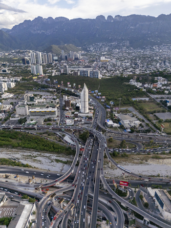 Aerial view of a complex highway interchange with heavy traffic surrounded by modern urban buildings and the dramatic backdrop of the mountains in Monterrey Nuevo Leon Mexico. Aerial view of a complex highway interchange with heavy traffic surrounded by modern urban buildings and the dramatic backdrop of the mountains in Monterrey Nuevo Leon Mexico.