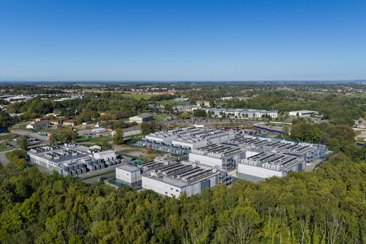 Aerial view of a data center facility surrounded by lush green trees and open landscape United Kingdom.