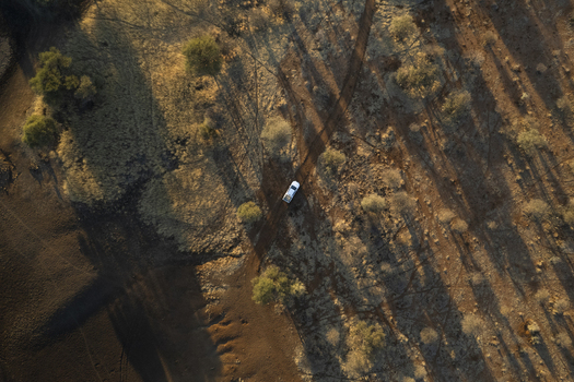 Aerial view of a lone white vehicle traversing the vast sun scorched landscape casting long shadows across the rugged terrain Windhoek Namibia. Aerial view of a lone white vehicle traversing the vast sun scorched landscape casting long shadows across the rugged terrain Windhoek Namibia.