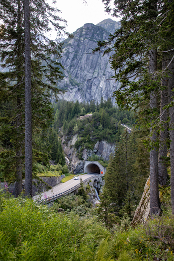 View of a road tunnel entrance nestled within the rocky cliffs and pine forests of the Swiss Alps in Airolo Ticino Switzerland. View of a road tunnel entrance nestled within the rocky cliffs and pine forests of the Swiss Alps in Airolo Ticino Switzerland.