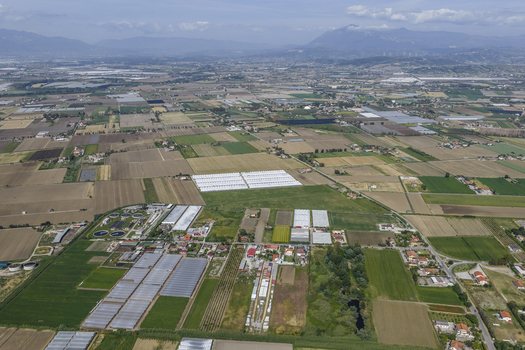 Aerial view of vast agricultural fields modern greenhouses and rural settlements under a clear sky with distant mountains in Paestum Campania Italy.