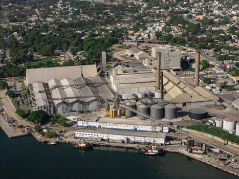 Aerial view of the industrial port facility with large warehouses storage silos and smokestacks along the waterfront Bajos de Haina San Cristobal Province Dominican Republic.