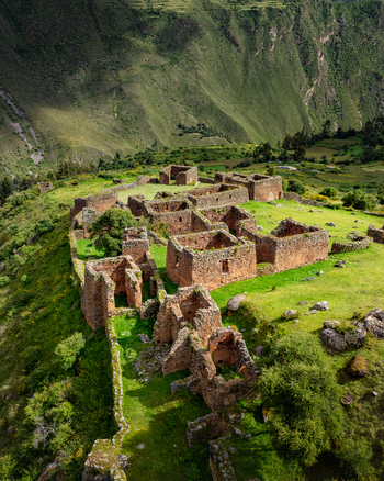 Aerial view of Pumamarca Ruins in the Sacred Valley featuring ancient stone walls and structures set against lush green hillsides in Pallata Qosqo Peru.