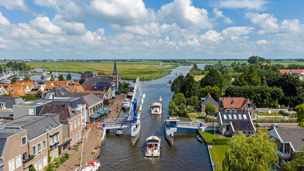 Aerial view of a drawbridge over a canal with boats passing through surrounded by historic brick buildings and green fields in Woudsend Friesland Netherlands. Aerial view of a drawbridge over a canal with boats passing through surrounded by historic brick buildings and green fields in Woudsend Friesland Netherlands.