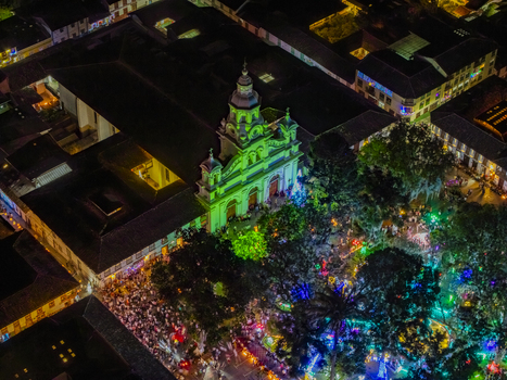 Aerial view of a vibrant plaza bustling with life under a canopy of trees illuminated with colorful lights framed by the glowing church Salamina Caldas Colombia. Aerial view of a vibrant plaza bustling with life under a canopy of trees illuminated with colorful lights framed by the glowing church Salamina Caldas Colombia.