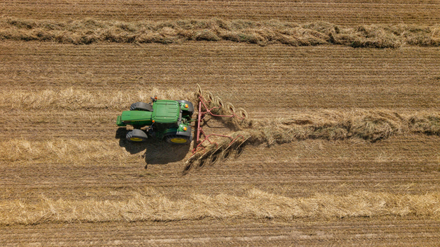 Aerial view of a green tractor pulling a hay rake across a harvested field in Philadelphia Western Cape South Africa. Aerial view of a green tractor pulling a hay rake across a harvested field in Philadelphia Western Cape South Africa.
