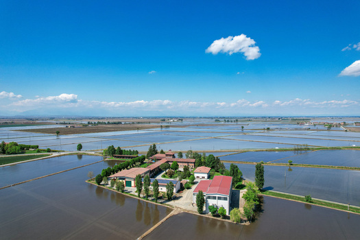 Aerial view of Abbazia di Lucedio surrounded by flooded rice fields and rural buildings under a blue sky Trino Piemonte Italy.