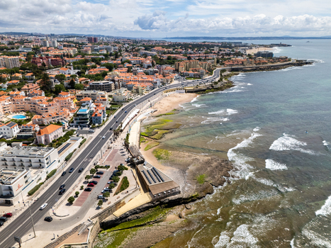 Aerial view of Avenida Marginal winding along the rocky coastline with waves crashing on the shore and urban buildings under a cloudy sky in Parede Lisboa Portugal. Aerial view of Avenida Marginal winding along the rocky coastline with waves crashing on the shore and urban buildings under a cloudy sky in Parede Lisboa Portugal.