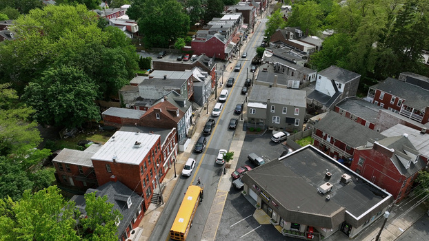 Aerial view of a yellow school bus driving down a street lined with historic brick buildings and lush green trees in South Lancaster Lancaster Pennsylvania United States. Aerial view of a yellow school bus driving down a street lined with historic brick buildings and lush green trees in South Lancaster Lancaster Pennsylvania United States.