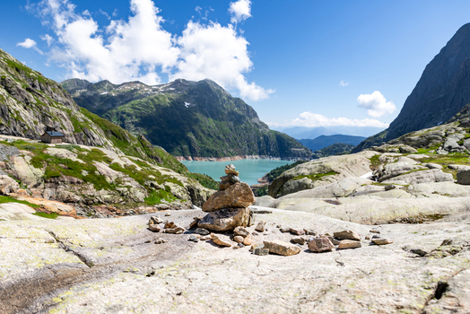 View of VerticAlp Emosson with a stone cairn on rocky terrain overlooking the turquoise Lac d Emosson and alpine mountains under a blue sky in Le Chatelard Fribourg Switzerland. View of VerticAlp Emosson with a stone cairn on rocky terrain overlooking the turquoise Lac d Emosson and alpine mountains under a blue sky in Le Chatelard Fribourg Switzerland.
