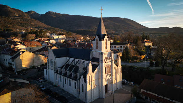 Aerial view of the historic Eglise Saint Pierre with its tall steeple and surrounding town rooftops against the Jura mountains at sunset in Gex Auvergne Rhone Alpes France. Aerial view of the historic Eglise Saint Pierre with its tall steeple and surrounding town rooftops against the Jura mountains at sunset in Gex Auvergne Rhone Alpes France.