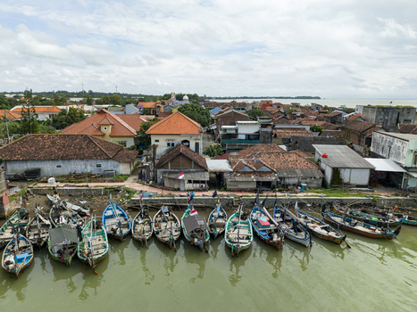 Aerial view of colorful boats clustered along the Jepara Floating Fish Market contrasting with the earthy tones of the buildings and the sea Jepara Central Java Indonesia.