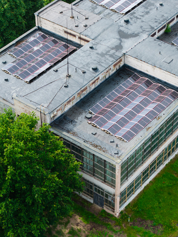 Aerial view of a building featuring solar panels installed on its flat roof surrounded by lush green trees and grass in an industrial area in Olaine Olaine Municipality Latvia. Aerial view of a building featuring solar panels installed on its flat roof surrounded by lush green trees and grass in an industrial area in Olaine Olaine Municipality Latvia.