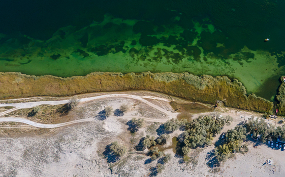 Aerial view of Blind Lake Sarfaranga Shigar with clear green water sandy shoreline and dirt tracks in Skardu Gilgit Pakistan.