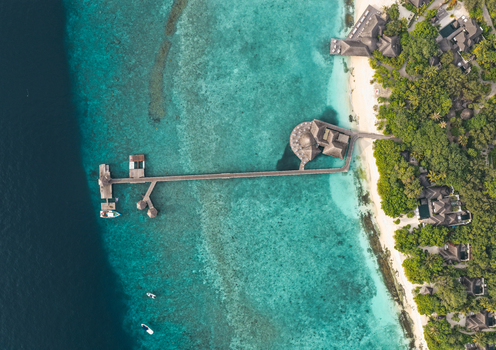 Aerial view of a luxury resort with a wooden jetty extending over turquoise waters and coral reefs in Hoarafushi Haa Alif Atoll Maldives. Aerial view of a luxury resort with a wooden jetty extending over turquoise waters and coral reefs in Hoarafushi Haa Alif Atoll Maldives.