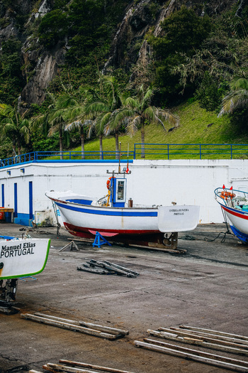 View of small fishing boats resting on the concrete ground against a backdrop of verdant cliffs the scene imbued with a tranquil coastal charm São Miguel Portugal. View of small fishing boats resting on the concrete ground against a backdrop of verdant cliffs the scene imbued with a tranquil coastal charm São Miguel Portugal.