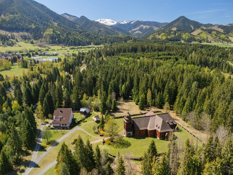 Aerial view of the Wooden Articular Church of Svaty Kriz surrounded by pine forests and rolling green hills with snow capped mountains Svaty Kriz Zilinsky kraj Slovakia.