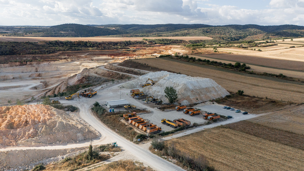 Aerial view of the Besenovo quarry showing heavy machinery excavators and dump trucks working on the site surrounded by fields and hills under a cloudy sky. Besenovo Vojvodina Serbia. Aerial view of the Besenovo quarry showing heavy machinery excavators and dump trucks working on the site surrounded by fields and hills under a cloudy sky. Besenovo Vojvodina Serbia.