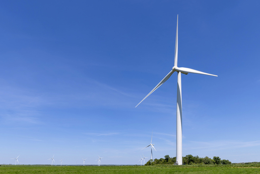 View of modern wind turbines standing in a lush green field under a clear blue sky Toronto Ontario Canada.