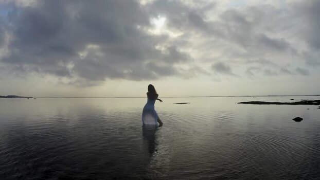 Aerial view of a woman in a white dress dancing in the ocean Indonesia.