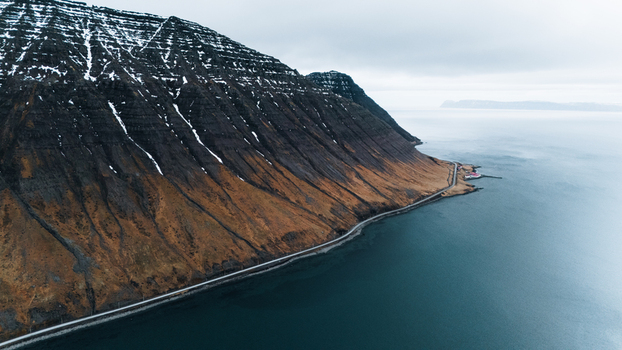 Aerial view of a dramatic coastline where rugged mountains meet the serene sea a road winding along the edge contrasting earth tones with the cool ocean Ísafjörður Iceland. Aerial view of a dramatic coastline where rugged mountains meet the serene sea a road winding along the edge contrasting earth tones with the cool ocean Ísafjörður Iceland.