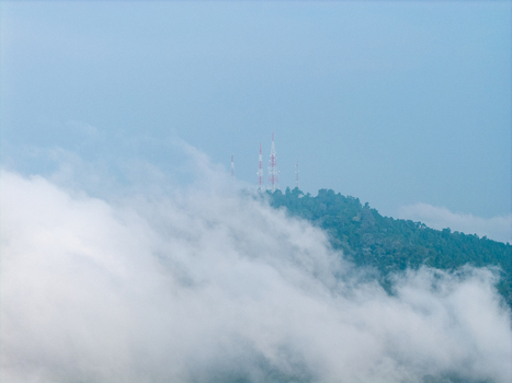 Aerial view of communication towers atop a lush tropical rainforest hill shrouded in thick morning mist under a clear blue sky in Bukit Mertajam Penang Malaysia. Aerial view of communication towers atop a lush tropical rainforest hill shrouded in thick morning mist under a clear blue sky in Bukit Mertajam Penang Malaysia.