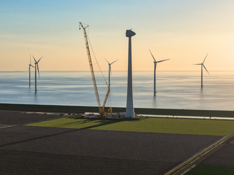 Aerial view of an offshore wind farm construction site with a large yellow crane and wind turbines standing in the sea at sunset Netherlands.