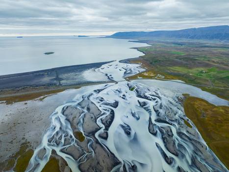 Aerial view of glacial rivers carving intricate patterns across the volcanic plains contrasting starkly with the distant ocean Iceland Iceland. Aerial view of glacial rivers carving intricate patterns across the volcanic plains contrasting starkly with the distant ocean Iceland Iceland.