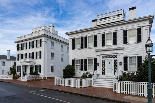 View of historic white houses with black shutters and picket fences along a brick sidewalk in Martha s Vineyard Edgartown Massachusetts United States.