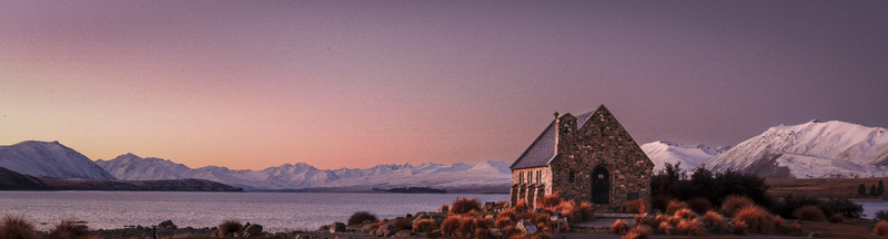 View of the Church of the Good Shepherd on the shore of Lake Tekapo with snow capped Southern Alps in the background under a vibrant sunset sky Lake Tekapo Canterbury Region New Zealand.