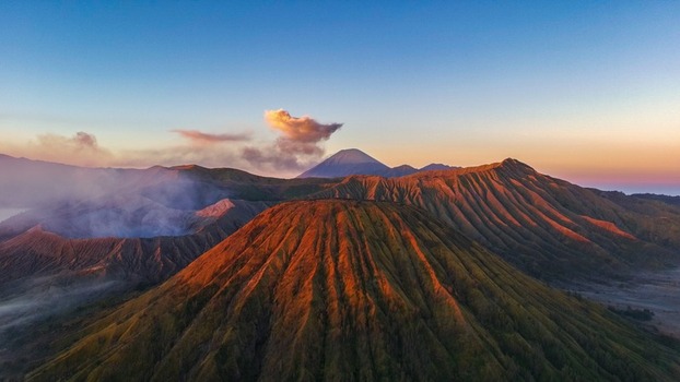Aerial view of Mount Bromo with its smoking crater and rugged volcanic ridges illuminated by the warm light of golden hour in Tosari East Java Indonesia.