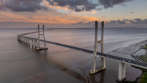 Aerial view of the Vasco da Gama Bridge spanning the Tagus River under a dramatic sunset sky with colorful clouds in Lisboa Portugal.