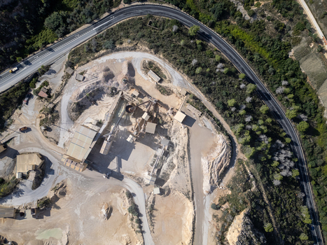 Aerial view of a stone quarry with industrial processing machinery gravel piles and access roads surrounded by vegetation and a highway in Teulada Valencian Community Spain.