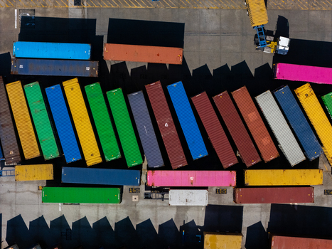 Aerial view of colorful shipping containers arranged in a busy logistics yard with industrial equipment and paved ground in Carson California United States.