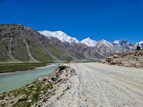 View of Penzi La road running alongside a river with snow capped mountains in the background under a clear blue sky in Zanskar Ladakh India.