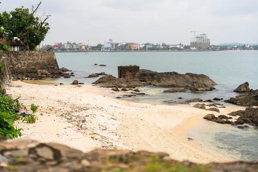 View of the historic Galle Fort walls and a sandy beach with plastic litter and rocky outcrops overlooking the bay Galle Southern Province Sri Lanka.