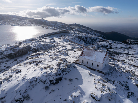 Aerial view of a snow dusted landscape with a solitary white building overlooking a serene lake reflecting the sky Lagoa Comprida São Romão Serra da Estrella Portugal. Aerial view of a snow dusted landscape with a solitary white building overlooking a serene lake reflecting the sky Lagoa Comprida São Romão Serra da Estrella Portugal.