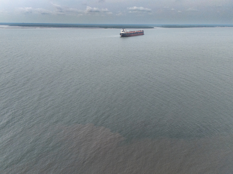 Aerial view of a large cargo ship navigating the waters near Bonny Island with visible sediment plumes in the river delta Bonny Town Rivers Nigeria. Aerial view of a large cargo ship navigating the waters near Bonny Island with visible sediment plumes in the river delta Bonny Town Rivers Nigeria.