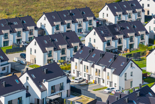 Aerial view of a modern residential housing development featuring rows of white houses with dark tiled roofs driveways and green lawns in Gdansk Pomeranian Voivodeship Poland. Aerial view of a modern residential housing development featuring rows of white houses with dark tiled roofs driveways and green lawns in Gdansk Pomeranian Voivodeship Poland.